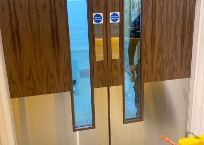 Timber-veneer fire doors with stainless steel kick plates being fitted in NEXT store"