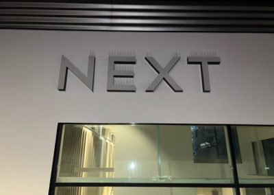 Close-up of rendered shopfront wall with NEXT signage and glass entrance