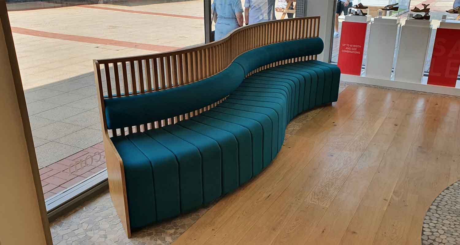 Curved oak-framed bench seating with teal upholstery and slatted backrest, bespoke joinery by Central Shop Maintenance for a retail unit